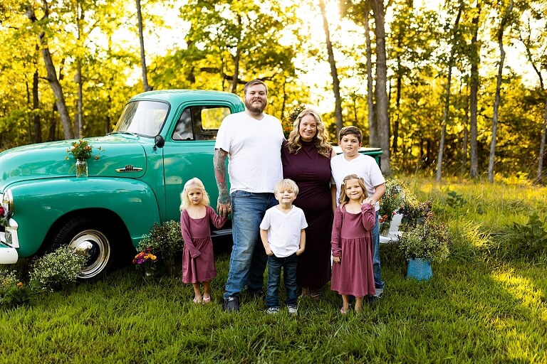 Blended family near teal vintage truck and fresh wildflowers in High Hill Missouri at golden hour