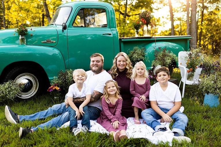 Blended family near teal vintage truck and fresh wildflowers in High Hill Missouri at golden hour