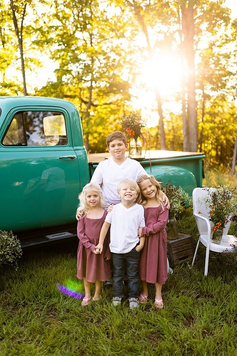 Blended family near teal vintage truck and fresh wildflowers in High Hill Missouri at golden hour