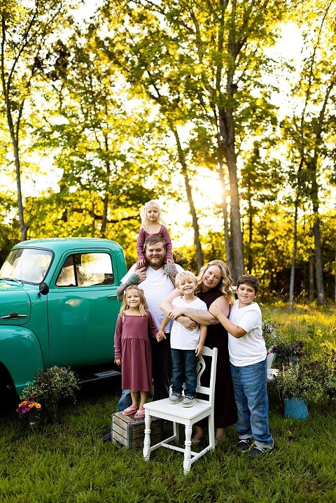 Blended family near teal vintage truck and fresh wildflowers in High Hill Missouri at golden hour