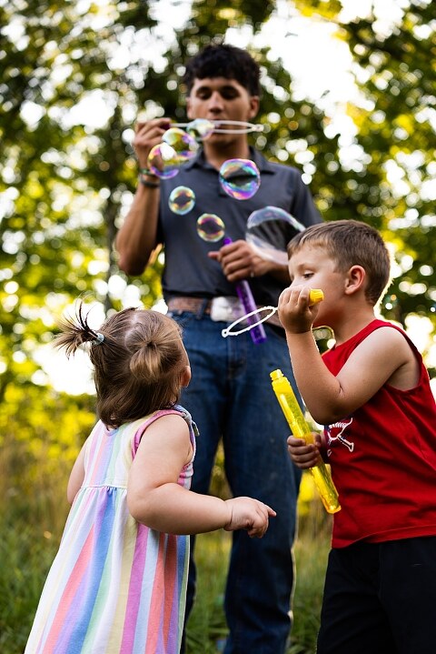 Playful family photo session in High Hill Missouri with mom and four kids enjoying bubbles, sprinkler fun, mud, and sunshine during summertime minis.