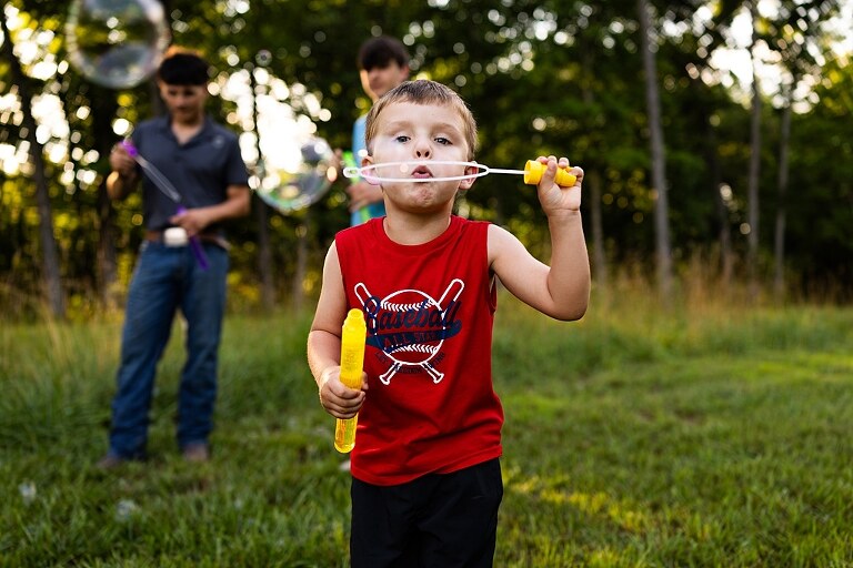 Playful family photo session in High Hill Missouri with mom and four kids enjoying bubbles, sprinkler fun, mud, and sunshine during summertime minis.