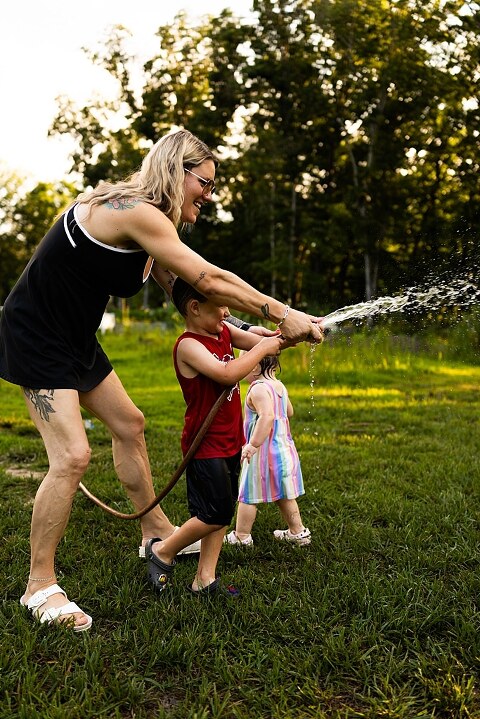 Playful family photo session in High Hill Missouri with mom and four kids enjoying bubbles, sprinkler fun, mud, and sunshine during summertime minis.