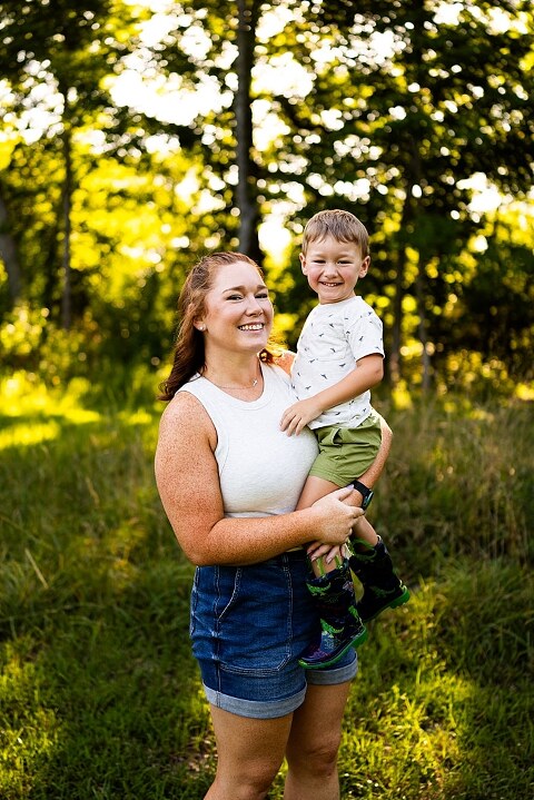 Mom and young son laughing and playing together outdoors during summertime mini session, splashing in water, chasing bubbles, and making unforgettable memories.