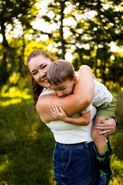 Mom and young son laughing and playing together outdoors during summertime mini session, splashing in water, chasing bubbles, and making unforgettable memories.