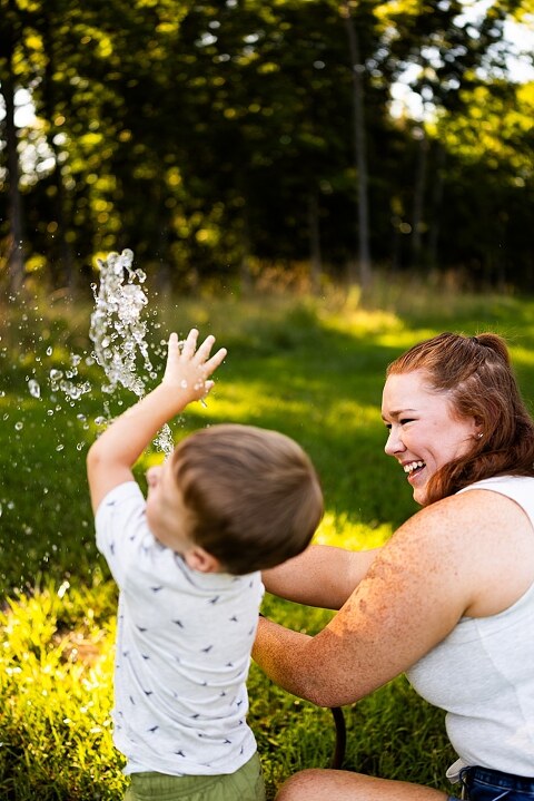 Mom and young son laughing and playing together outdoors during summertime mini session, splashing in water, chasing bubbles, and making unforgettable memories.