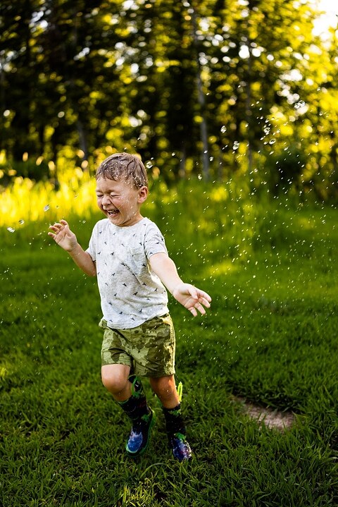 Mom and young son laughing and playing together outdoors during summertime mini session, splashing in water, chasing bubbles, and making unforgettable memories.