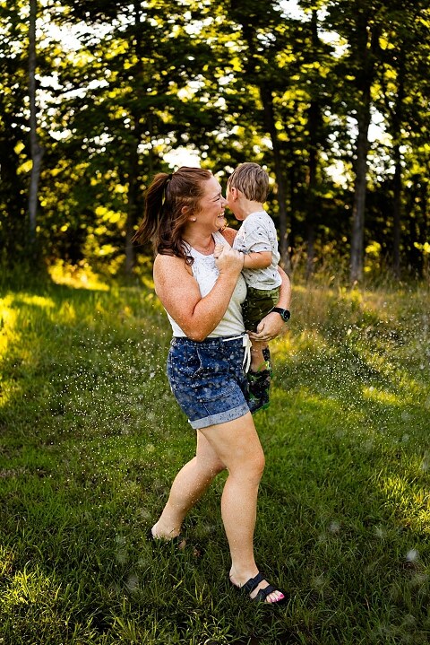 Mom and young son laughing and playing together outdoors during summertime mini session, splashing in water, chasing bubbles, and making unforgettable memories.