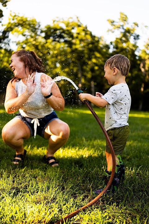 Mom and young son laughing and playing together outdoors during summertime mini session, splashing in water, chasing bubbles, and making unforgettable memories.
