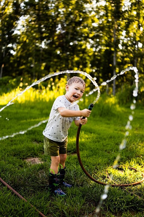 Mom and young son laughing and playing together outdoors during summertime mini session, splashing in water, chasing bubbles, and making unforgettable memories.
