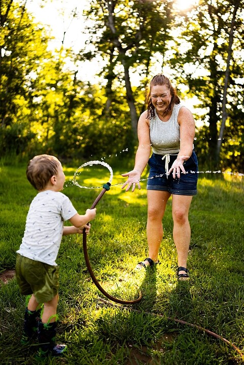 Mom and young son laughing and playing together outdoors during summertime mini session, splashing in water, chasing bubbles, and making unforgettable memories.