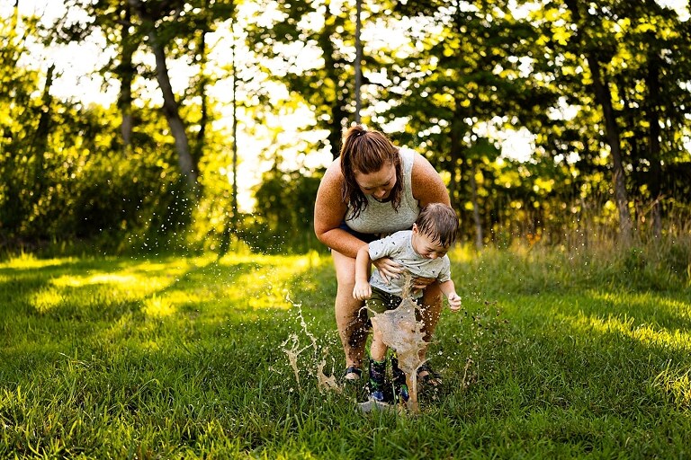Mom and young son laughing and playing together outdoors during summertime mini session, splashing in water, chasing bubbles, and making unforgettable memories.