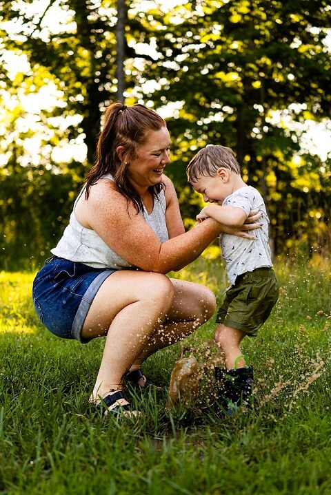 Mom and young son laughing and playing together outdoors during summertime mini session, splashing in water, chasing bubbles, and making unforgettable memories.