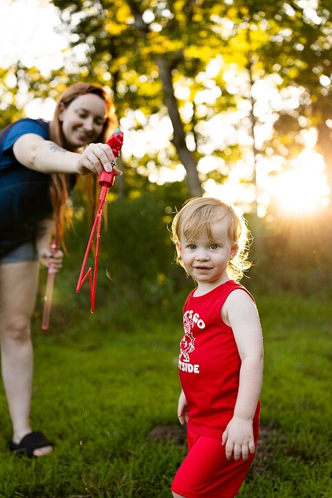 Family of four playing outdoors during summertime mini session, laughing, splashing water, blowing bubbles, and making joyful memories together.