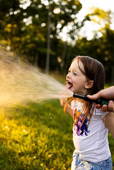 Family of four playing outdoors during summertime mini session, laughing, splashing water, blowing bubbles, and making joyful memories together.
