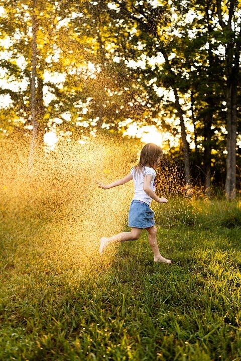 Family of four playing outdoors during summertime mini session, laughing, splashing water, blowing bubbles, and making joyful memories together.