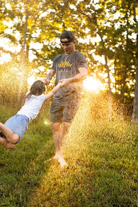 Family of four playing outdoors during summertime mini session, laughing, splashing water, blowing bubbles, and making joyful memories together.