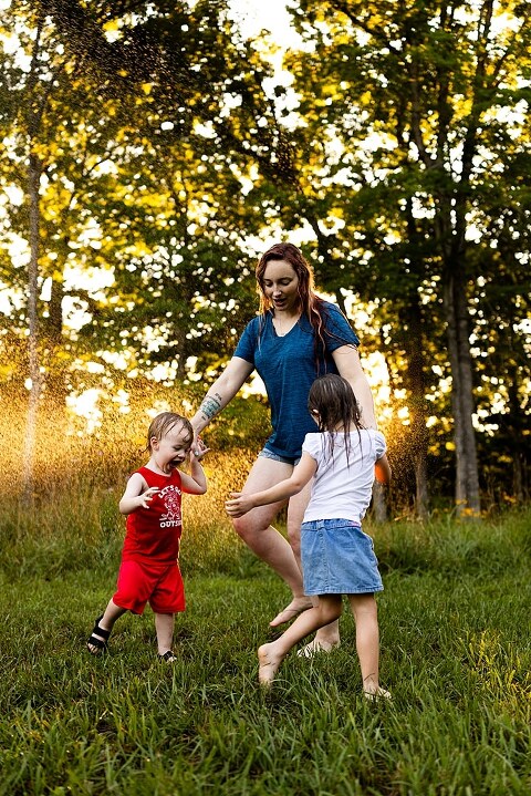 Family of four playing outdoors during summertime mini session, laughing, splashing water, blowing bubbles, and making joyful memories together.