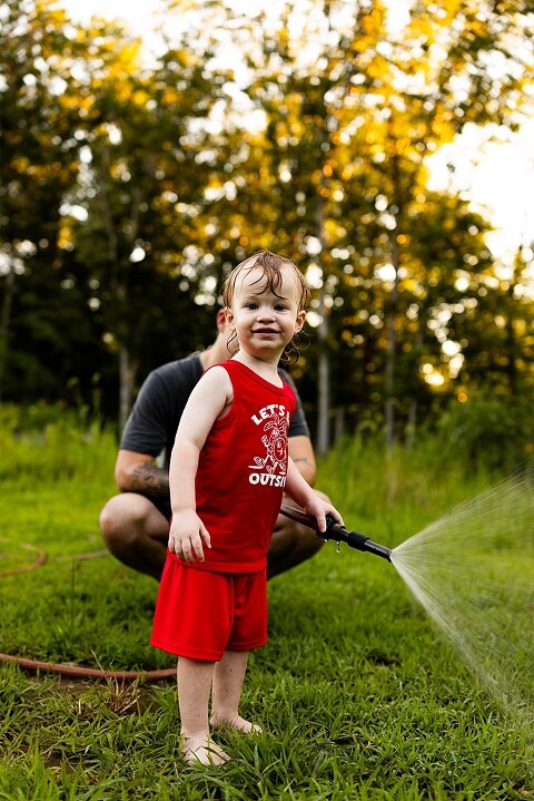 Family of four playing outdoors during summertime mini session, laughing, splashing water, blowing bubbles, and making joyful memories together.