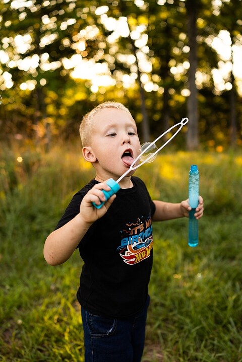 Mom and young son playing together outdoors during summertime mini session, blowing bubbles, splashing water, and sharing joyful moments in the sunshine.