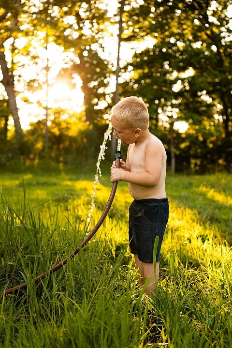 Mom and young son playing together outdoors during summertime mini session, blowing bubbles, splashing water, and sharing joyful moments in the sunshine.