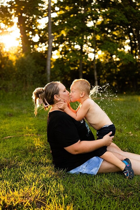 Mom and young son playing together outdoors during summertime mini session, blowing bubbles, splashing water, and sharing joyful moments in the sunshine.