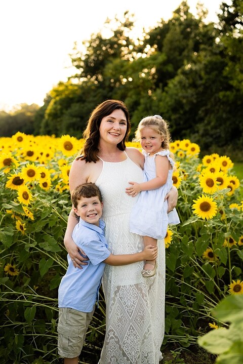 Family of four during sunflower mini photo session in Jonesburg Missouri | Kids smiling in sunflower field during family tradition photo shoot | Family cuddles in sunflower field during summer photos | Missouri Photographer | Outdoor photographer 