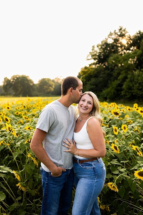Extended family standing together in a sunflower field smiling during a summer mini session | Grandparents surrounded by their grandchildren in a bright sunflower patch | Large family group walking through sunflowers during a summer photo session