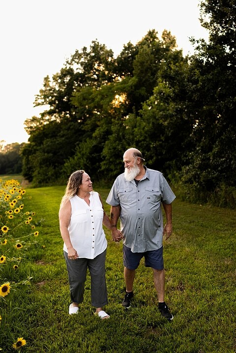 Extended family standing together in a sunflower field smiling during a summer mini session | Grandparents surrounded by their grandchildren in a bright sunflower patch | Large family group walking through sunflowers during a summer photo session