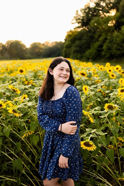 Extended family standing together in a sunflower field smiling during a summer mini session | Grandparents surrounded by their grandchildren in a bright sunflower patch | Large family group walking through sunflowers during a summer photo session