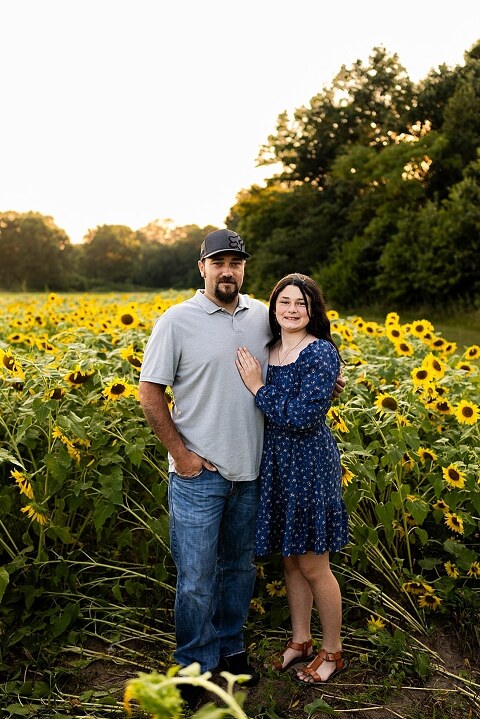Extended family standing together in a sunflower field smiling during a summer mini session | Grandparents surrounded by their grandchildren in a bright sunflower patch | Large family group walking through sunflowers during a summer photo session