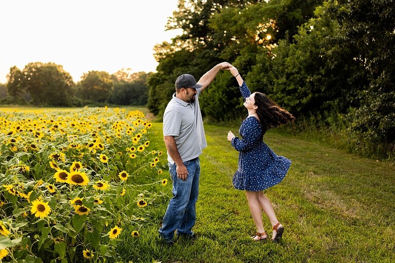 Extended family standing together in a sunflower field smiling during a summer mini session | Grandparents surrounded by their grandchildren in a bright sunflower patch | Large family group walking through sunflowers during a summer photo session