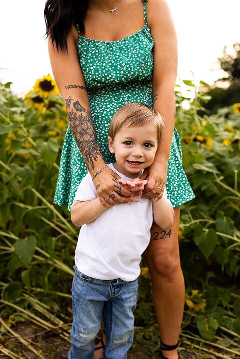 Family of three smiling together in a bright sunflower field during summer | Little boy grinning while standing among tall sunflowers
 | Parents holding their son and laughing in golden evening light | Family hugging closely surrounded by blooming sunflowers
