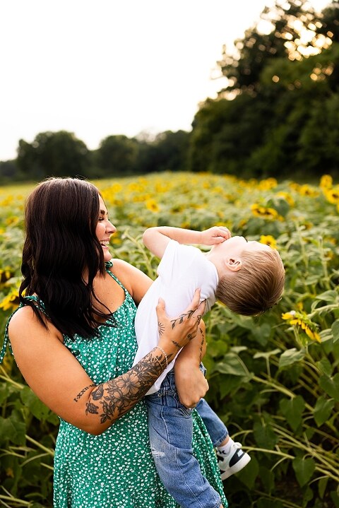 Family of three smiling together in a bright sunflower field during summer | Little boy grinning while standing among tall sunflowers
 | Parents holding their son and laughing in golden evening light | Family hugging closely surrounded by blooming sunflowers
