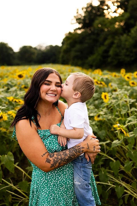 Family of three smiling together in a bright sunflower field during summer | Little boy grinning while standing among tall sunflowers
 | Parents holding their son and laughing in golden evening light | Family hugging closely surrounded by blooming sunflowers