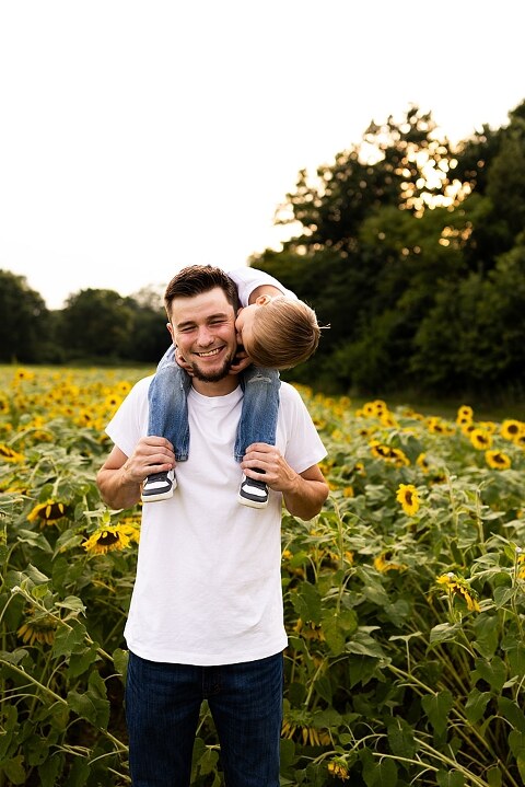 Family of three smiling together in a bright sunflower field during summer | Little boy grinning while standing among tall sunflowers
 | Parents holding their son and laughing in golden evening light | Family hugging closely surrounded by blooming sunflowers