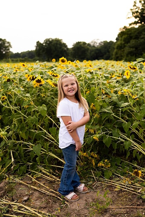 Blended family smiling together in a sunflower field during a summer mini session | Mom and children laughing among tall sunflowers in warm evening light | Parents holding hands and smiling in a bright sunflower patch | Close up of family hugging with golden blooms surrounding them