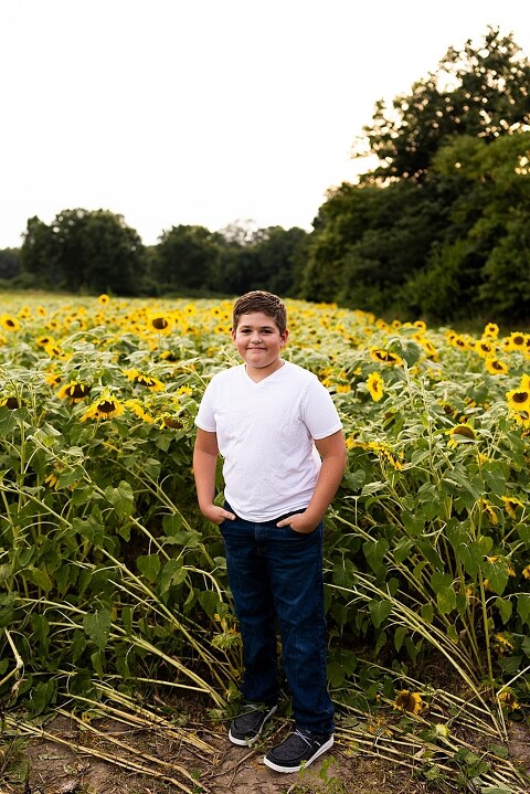 Blended family smiling together in a sunflower field during a summer mini session | Mom and children laughing among tall sunflowers in warm evening light | Parents holding hands and smiling in a bright sunflower patch | Close up of family hugging with golden blooms surrounding them