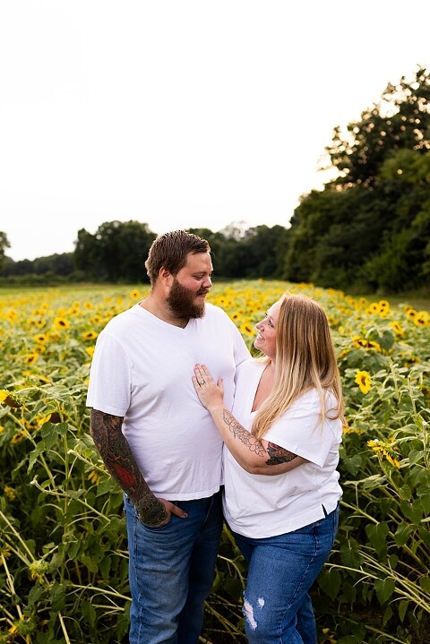 Blended family smiling together in a sunflower field during a summer mini session | Mom and children laughing among tall sunflowers in warm evening light | Parents holding hands and smiling in a bright sunflower patch | Close up of family hugging with golden blooms surrounding them