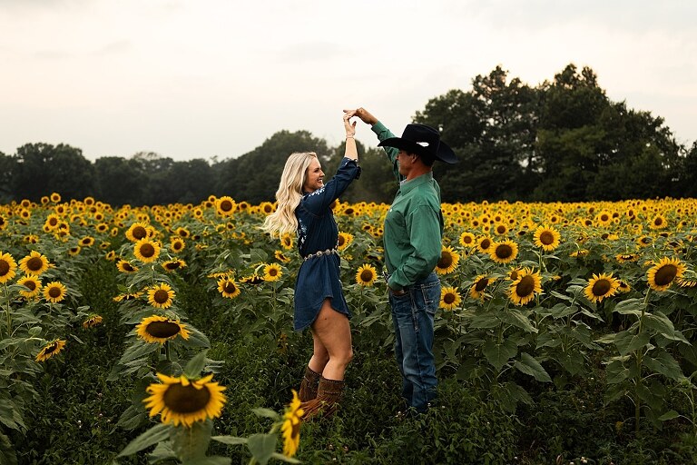 Couple standing together in a sunflower field during sunset in Jonesburg Missouri | Dog sitting in front of sunflowers with golden evening light | Couple laughing while holding their dog in a sunflower field | Sunflower Mini Photo Shoot with couple and dog at golden hour | Dog running through sunflower rows during family photo session | Missouri Sunflower Photographer