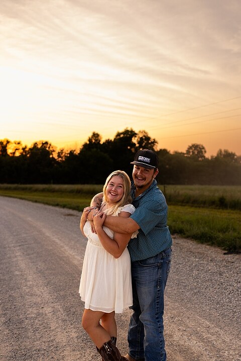 Couple walking hand in hand down a gravel road at sunset | Woman smiling at her partner during a country photo session | Former Missouri State Fair Queen posing with her partner in soft evening light | Close up of couple laughing while standing on a quiet country road