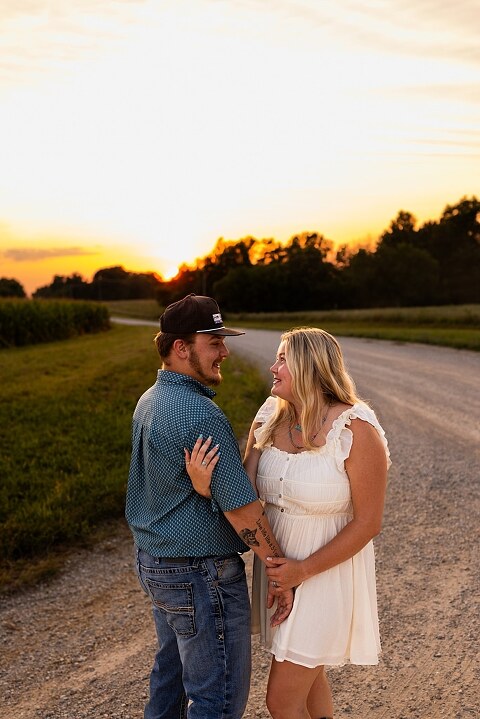 Couple walking hand in hand down a gravel road at sunset | Woman smiling at her partner during a country photo session | Former Missouri State Fair Queen posing with her partner in soft evening light | Close up of couple laughing while standing on a quiet country road
