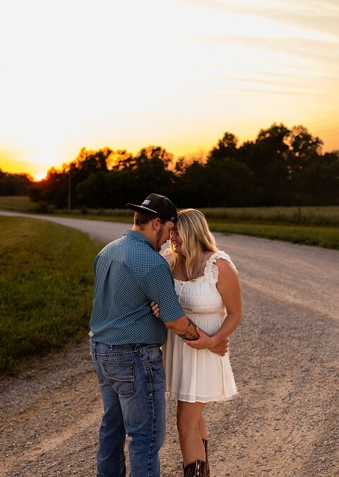 Couple walking hand in hand down a gravel road at sunset | Woman smiling at her partner during a country photo session | Former Missouri State Fair Queen posing with her partner in soft evening light | Close up of couple laughing while standing on a quiet country road