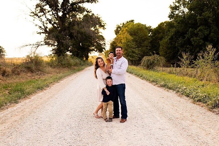 Oden Family walking together on a gravel road during a September photo session
Parents smiling at their children while standing on a country road
Children running and laughing down a gravel road in golden light
Family hugging closely with the soft glow of evening behind them