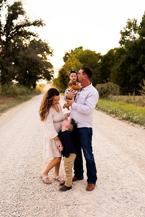 Oden Family walking together on a gravel road during a September photo session
Parents smiling at their children while standing on a country road
Children running and laughing down a gravel road in golden light
Family hugging closely with the soft glow of evening behind them