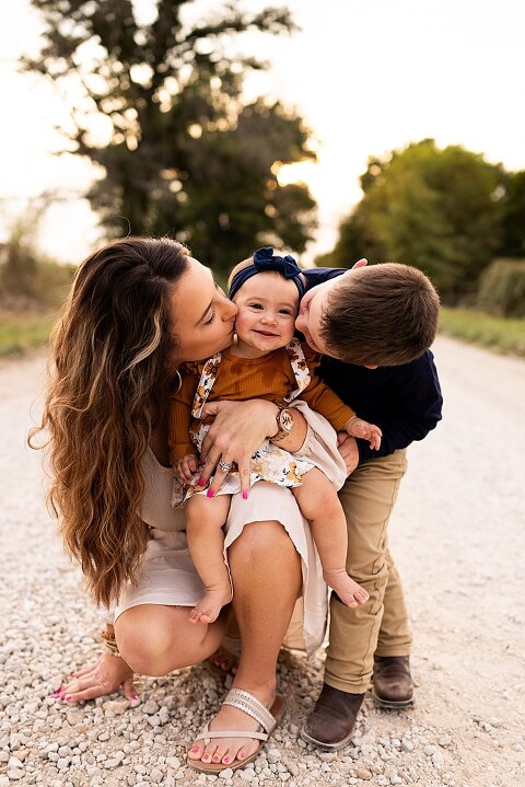 Oden Family walking together on a gravel road during a September photo session
Parents smiling at their children while standing on a country road
Children running and laughing down a gravel road in golden light
Family hugging closely with the soft glow of evening behind them