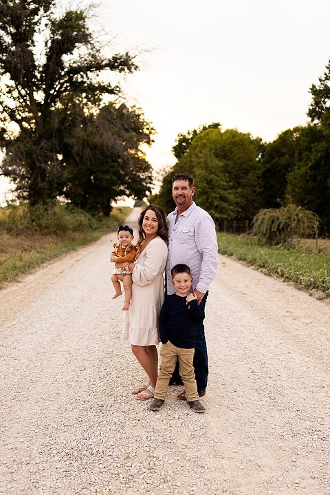 Oden Family walking together on a gravel road during a September photo session
Parents smiling at their children while standing on a country road
Children running and laughing down a gravel road in golden light
Family hugging closely with the soft glow of evening behind them