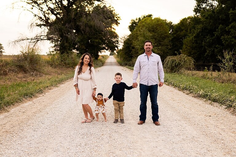 Oden Family walking together on a gravel road during a September photo session
Parents smiling at their children while standing on a country road
Children running and laughing down a gravel road in golden light
Family hugging closely with the soft glow of evening behind them