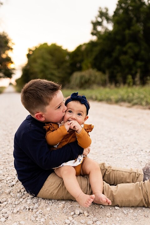 Oden Family walking together on a gravel road during a September photo session
Parents smiling at their children while standing on a country road
Children running and laughing down a gravel road in golden light
Family hugging closely with the soft glow of evening behind them