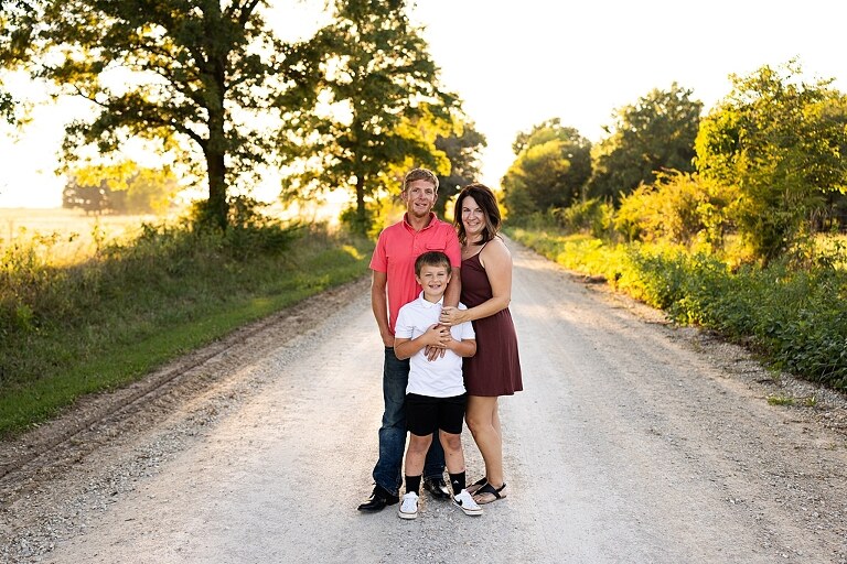 Family walking together through a field in High Hill Missouri
Parents smiling at their child while standing on a gravel road
Child laughing and making a silly face during a family session
Family holding hands in tall grass with warm evening light
Parents hugging their child while standing on a quiet country road